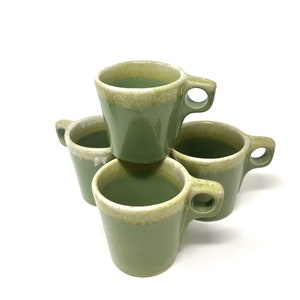 May include: Set of four green ceramic coffee mugs with a white glaze around the rim. The mugs are stacked on top of each other.