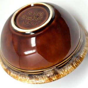 May include: A brown ceramic bowl with a glossy finish. The bowl has a white rim and a textured, tan-colored base. The underside of the bowl features the text "hull Oven Proof U.S.A."