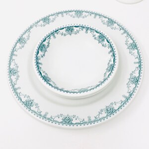 Może przedstawiać: Biały ceramiczny talerz obiadowy i mniejsza biała ceramiczna miska z zielonym wzorem kwiatowym wok&oacute;ł krawędzi.