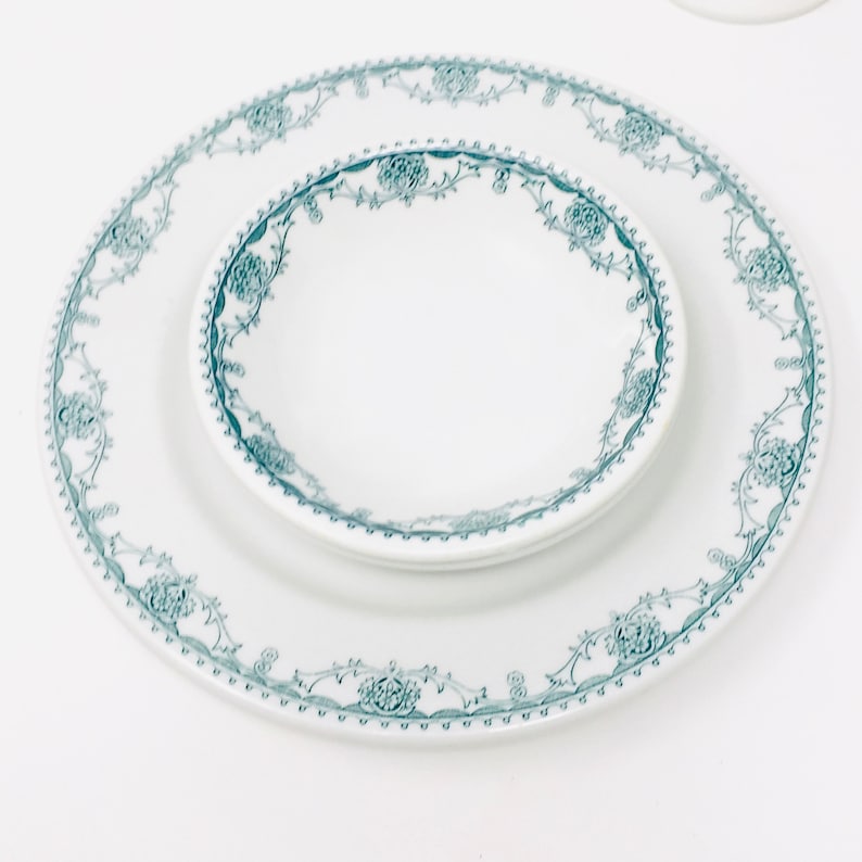 Może przedstawiać: Biały ceramiczny talerz obiadowy i mniejsza biała ceramiczna miska z zielonym wzorem kwiatowym wok&oacute;ł krawędzi.