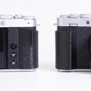 Könnte beinhalten: Zwei silberne und schwarze Digitalkameras werden nebeneinander vor einem weißen Hintergrund gezeigt. Die Kamera links hat einen Bildschirm und Tasten mit der Aufschrift "MENU OK" und "DISP BACK". Die Kamera rechts hat ein Objektiv.