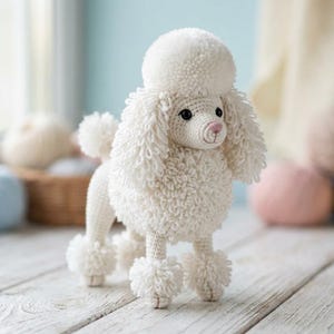 May include: A handmade white crochet poodle dog with a fluffy head, ears, and tail. The dog has black eyes and a pink nose. The poodle is standing on a wooden surface, with yarn balls in the background. A charming, handcrafted item.