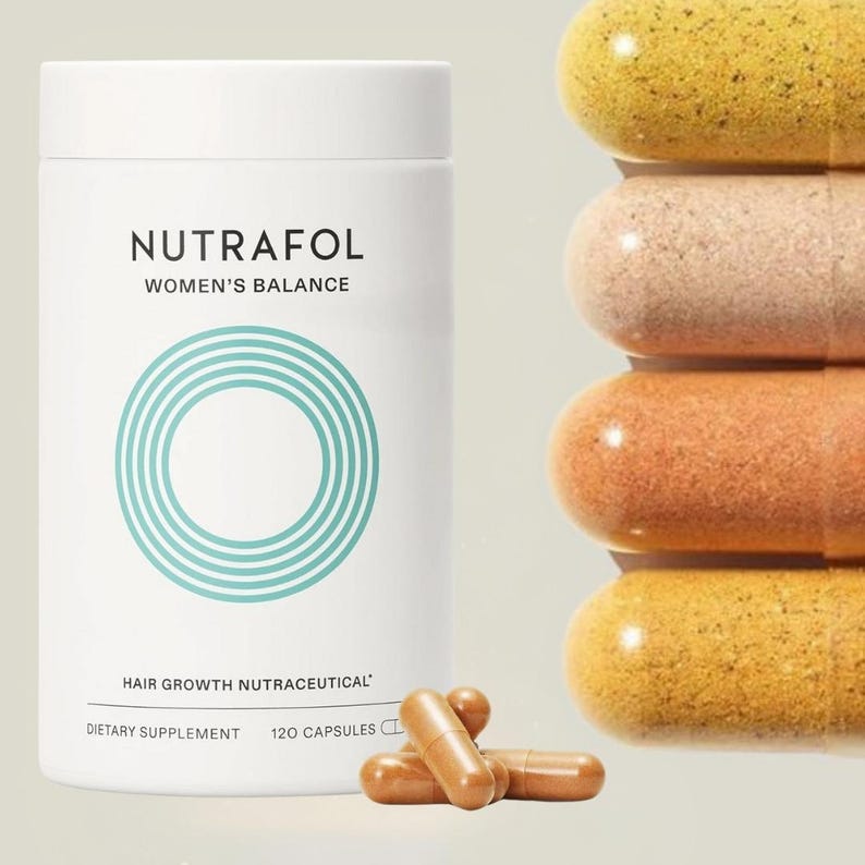 May include: A white bottle of Nutrafol Women's Balance hair growth supplement with a teal circular design. The bottle is next to a stack of capsules in shades of yellow, peach, and brown, and a few loose capsules.