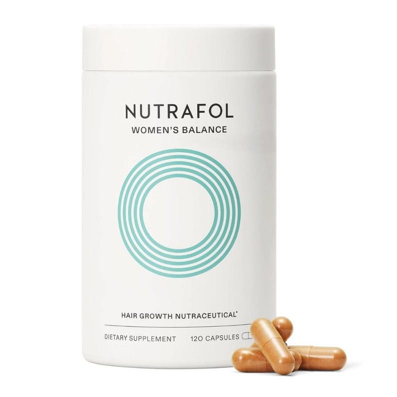 May include: A white cylindrical bottle of Nutrafol Women's Balance hair growth nutraceutical dietary supplement. The bottle has a teal circular design and text. Several brown capsules are scattered in front of the bottle.