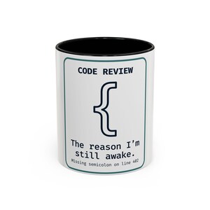Pode incluir: Caneca de cerâmica branca com interior preto. A caneca apresenta o texto "CODE REVIEW" acima de um símbolo de chave e a frase "The reason I'm still awake. Missing semicolon on line 402."
