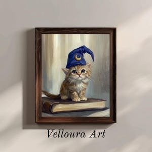 May include: A framed painting of a kitten wearing a blue wizard hat with a crescent moon. The kitten is sitting on a book. The artwork is signed "Velloura Art" in the bottom left corner.