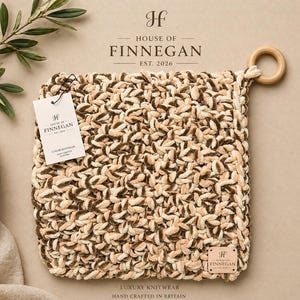 Op de afbeelding: Een vierkant, beige en bruin gebreid item met een houten ring eraan. Het item heeft een label met de tekst "HOUSE OF FINNEGAN" en "LUXURY KNITWEAR HAND CRAFTED IN BRITAIN". De achtergrond is een neutrale beige kleur.