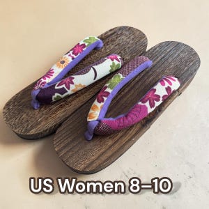 May include: Pair of wooden geta sandals with floral fabric straps in purple, white, and pink. The wooden base has a dark brown wood grain. The text "US Women 8-10" is at the bottom of the image.