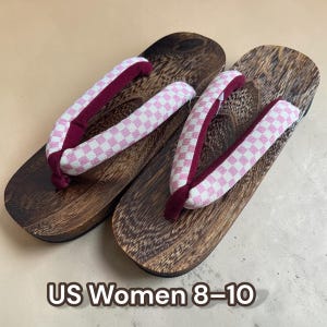 May include: Pair of wooden geta sandals with dark brown platforms and pink and white checkered straps. The straps are lined with a deep burgundy fabric. The text "US Women 8-10" is displayed at the bottom of the image.