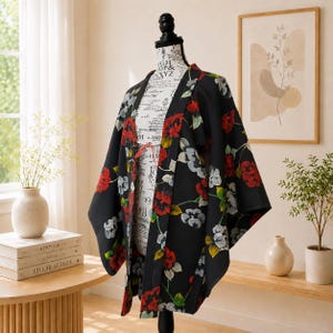 May include: A black kimono with a floral pattern of red, white, and yellow flowers. The kimono is displayed on a mannequin. The garment has wide sleeves and a loose, flowing design, perfect for layering or as a statement piece.