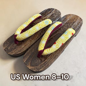 May include: Pair of wooden geta sandals with a dark wood grain finish. The straps are yellow with a white geometric pattern and a burgundy lining. The text "US Women 8-10" is visible.
