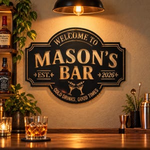 May include: A black metal wall sign with gold lettering that reads WELCOME TO MASON'S BAR EST. 2026 COLD DRINKS, GOOD TIMES. The sign features a decorative border and a graphic of two clinking martini glasses centred at the bottom of the text.
