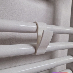 Puede incluir: Primer plano de un toallero blanco con un gancho de plástico blanco. El gancho está diseñado para sujetar toallas en el toallero. El toallero tiene varias barras horizontales.