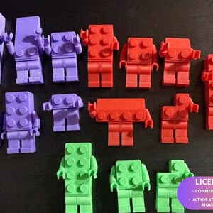 May include: A collection of purple, red, and green plastic toy figures shaped like building blocks with studs on their torsos and articulated arms. The figures vary in height and width, with some featuring full bodies and others appearing as partial torsos.