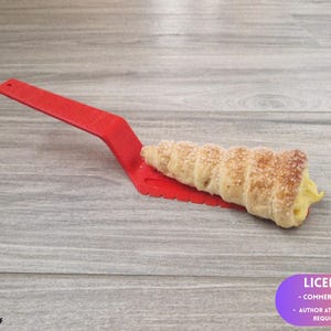 May include: A red plastic pastry server holding a cream horn pastry. The pastry is golden brown with a sugared exterior and a creamy yellow filling. The server is on a wooden surface.