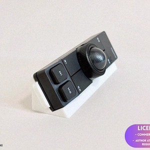 May include: A black rectangular macro keypad featuring a large circular dial, two square buttons labelled M1 and M2, and two smaller buttons labelled G1 and G2. The device is mounted on a white angled stand, providing an elevated viewing angle.