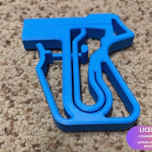 May include: A vibrant blue, 3D-printed spray bottle trigger. The design includes a handle, trigger, and nozzle. The object is placed on a textured, neutral-toned surface. The image includes a license notice.