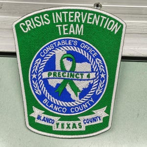 May include: A green and white embroidered patch with the text "CRISIS INTERVENTION TEAM" at the top. The center features a blue circle with a map of Texas and a green ribbon. The words "CONSTABLE'S OFFICE", "PRECINCT 4", "BLANCO COUNTY", and "TEXAS" are also visible.