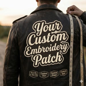 Peut inclure: Veste en cuir noir avec un grand écusson brodé dans le dos indiquant "Your Custom Embroidery Patch". En dessous, trois petits écussons avec du texte. Un mètre ruban est tenu contre la veste.