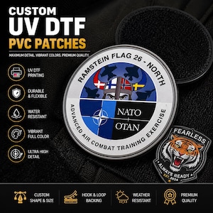 May include: A circular patch featuring the text RAMSTEIN FLAG 26 - NORTH and NATO OTAN with a central graphic of a helmeted figure and fighter jets. A smaller shield-shaped patch displays a tiger head with the text FEARLESS ALWAYS READY EST. 2024.