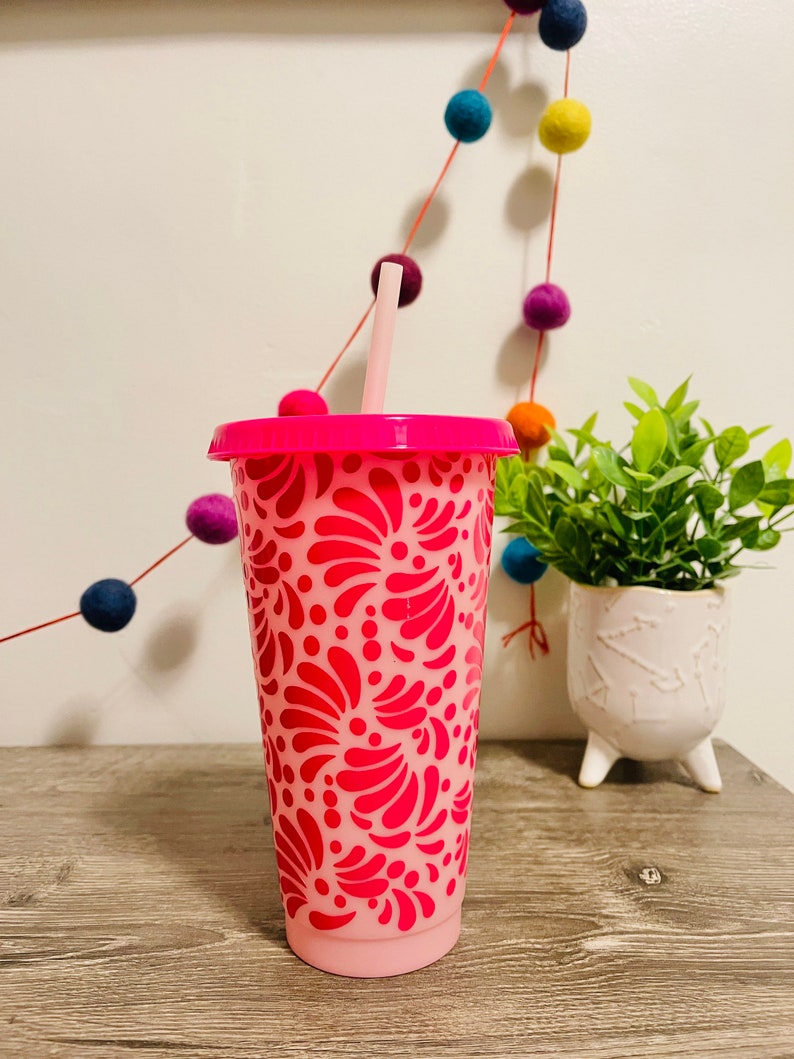 May include: A pink reusable tumbler with a pink and white floral design. The tumbler has a lid and a straw.