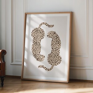 May include: A framed art print showing two stylized cheetahs in a neutral colour scheme. The cheetahs have black spots on a beige background, creating a modern and minimalist aesthetic. The artwork is framed in light wood.