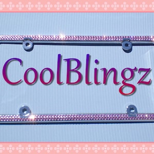 May include: A silver license plate frame with a pink rhinestone border. The frame has the text "CoolBlingz" in a purple and red gradient.