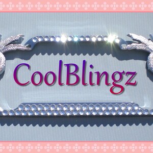 May include: Silver license plate frame with two palm tree designs on the sides. The frame is decorated with rhinestones and the text "CoolBlingz" is printed in the center.