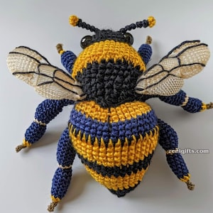 Puede incluir: Una abeja de ganchillo hecha a mano en amarillo, negro y azul. La abeja tiene alas, antenas y patas detalladas. El cuerpo está rayado con amarillo y negro, y las patas y la cabeza son azules. Las alas son de color crema.