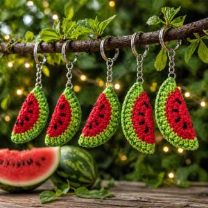 May include: Five handmade watermelon slice keychains with silver-colored keyrings hang from a tree branch. The keychains are red with black seed details and green rind. A watermelon slice and whole watermelon are in the foreground.