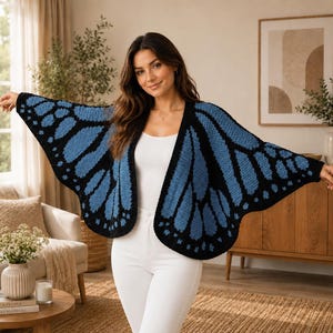 Puede incluir: Un cárdigan azul y negro con forma de ala de mariposa. El suéter abierto presenta un patrón de ala detallado en tonos azules y negros. El cárdigan está hecho de un material suave y tejido, perfecto para combinar.