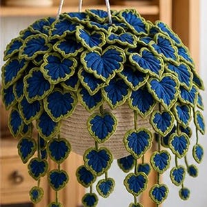 Peut inclure: Un pot suspendu avec un panier tressé et une cascade de feuilles crochetées bleues et vertes. Les feuilles en forme de cœur ont un centre bleu et un contour vert. Le pot est suspendu par une corde blanche.