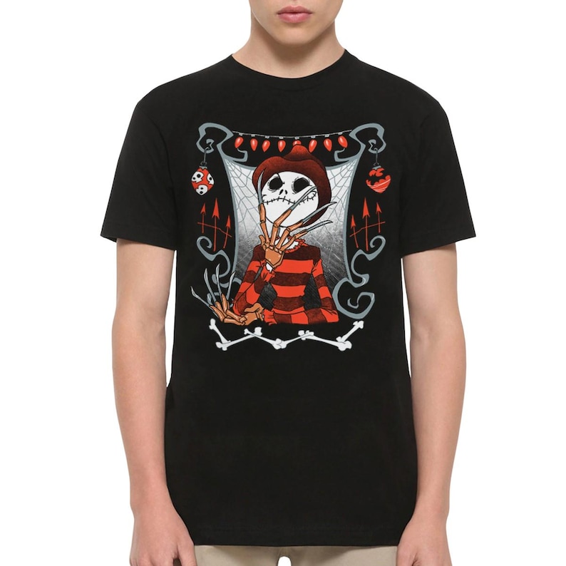 May include: A black short-sleeve t-shirt featuring a graphic print of a skeletal figure with long blade fingers, wearing a brown hat and a red and black striped sweater. The design includes a spiderweb background, red string lights, and bones.
