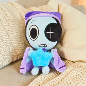 Puede incluir: Una mu&ntilde;eca de peluche con una cara azul claro, un ojo negro grande y un parche negro con una cruz blanca. Lleva un gorro de dormir y una capa morados, y sostiene una estrella azul. La mu&ntilde;eca est&aacute; dise&ntilde;ada para parecerse a un personaje de dibujos animados.