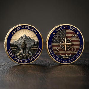 May include: Two gold-rimmed challenge coins with blue borders. The left coin shows a hiker facing mountains with text reading STAY FOCUSED, DISCIPLINE TODAY, SUCCESS TOMORROW, KEEP PUSHING FORWARD. The right coin features a compass, flag, and text.