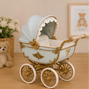 May include: A decorative baby carriage figurine in light blue with gold-toned accents and wheels. The carriage features a white interior, a scalloped white lace trim along the hood, and ornate gold filigree detailing on the exterior body.