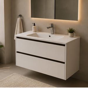 May include: A modern white floating bathroom vanity with two drawers and a rectangular integrated sink. A chrome tap, a small potted plant, and a soap dispenser sit on the countertop. A mirror with a warm light frame is above the vanity.