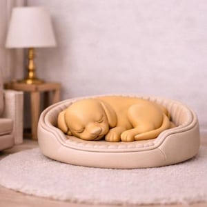 May include: A sleeping yellow puppy figurine in a beige dog bed. The bed has a stitched border and is placed on a white, fluffy rug. The puppy is curled up, eyes closed, in a relaxed pose.