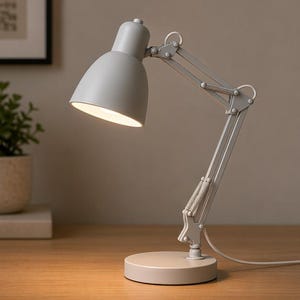 May include: A gray desk lamp with an adjustable arm and a round base. The lamp has a dome-shaped shade and a bright light. The lamp is on a wooden surface.