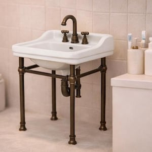 May include: A white porcelain sink with a bronze faucet and fixtures, supported by a bronze-colored metal frame. The sink is in a bathroom setting, with a white countertop and a tiled wall.