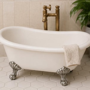 May include: A white clawfoot bathtub with a brass faucet and a beige towel. The tub has ornate silver feet and is set against a tiled wall and floor. A potted plant is visible in the background.
