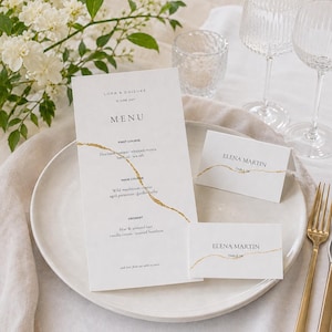 May include: A white wedding menu card and two place cards with gold foil accents, featuring the text Lora & Daisuke 15 June 2027, Menu, First Course, Main Course, Dessert, and Elena Martin Table 08, displayed on a ceramic plate with gold cutlery.