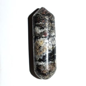 May include: A polished, double-terminated stone point featuring a mottled pattern of black, white, and deep red mineral inclusions. The cylindrical object has a smooth, glossy surface with a pointed top and a rounded base, displaying natural textures.