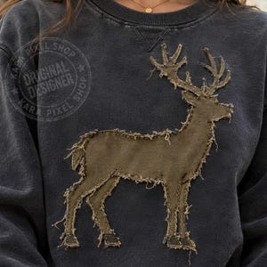 May include: A charcoal grey crewneck sweatshirt featuring a large, olive green deer silhouette appliqué on the front. The deer design has raw, frayed edges and visible stitching. A circular watermark with the text KARA PIXEL SHOP is visible.