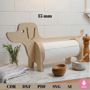May include: A wooden dachshund-shaped paper towel holder. The holder is made of light-colored wood and has a roll of white paper towels. The design includes the text "15 mm". The holder is on a countertop with other kitchen items.
