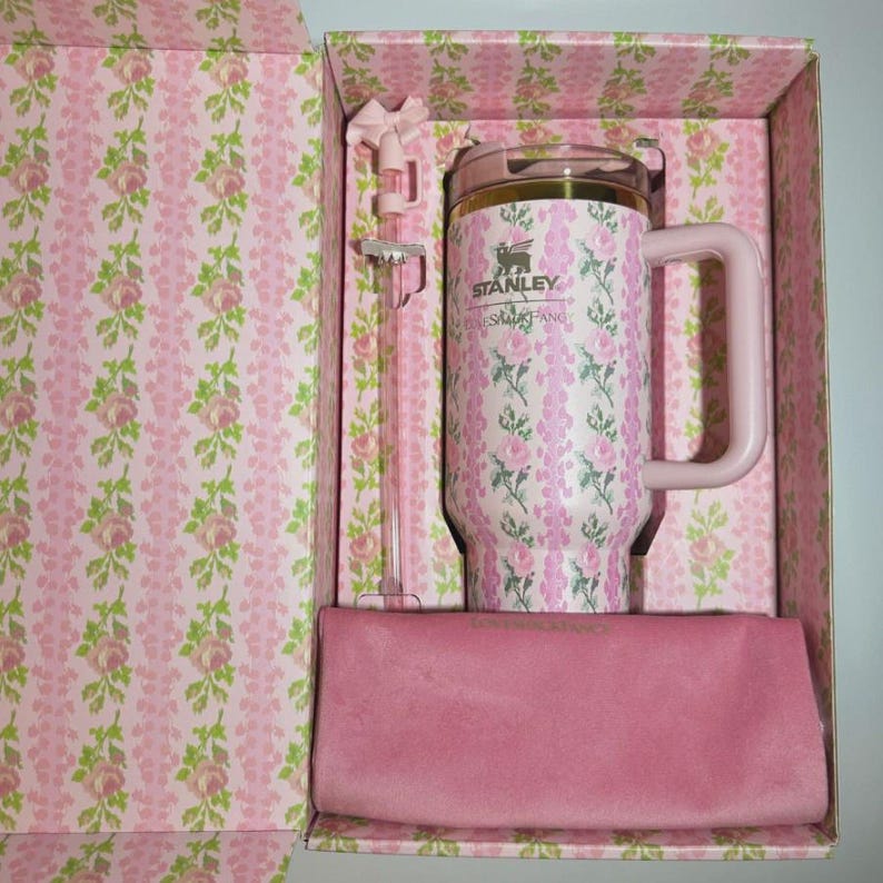 May include: A pink and white floral patterned Stanley tumbler with a matching straw and a solid pink rectangular cloth, all housed in a matching floral gift box. The tumbler features the Stanley logo and text printed on the front surface.