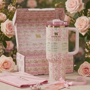 May include: A Stanley tumbler with a pink floral pattern, a matching box, a pink cloth pouch, and a small bow accessory. The tumbler features a handle, a clear lid with a straw, and the text Stanley and LoveShackFancy printed on the front label.