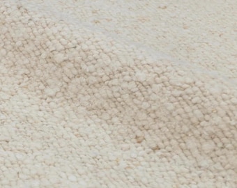 May include: Close-up of a textured, off-white rug. The rug has a thick, looped pile with subtle variations in color, creating a soft, inviting appearance. The neutral tones and tactile surface suggest a cozy, natural fiber rug.