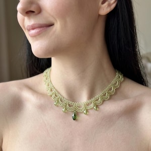 Puede incluir: Un collar de cuentas con un diseño festoneado en un tono verde oliva claro. La pieza está construida con pequeñas cuentas de semillas uniformes y está acentuada con varias cuentas colgantes en forma de lágrima facetada en un tono verde oliva más profundo.