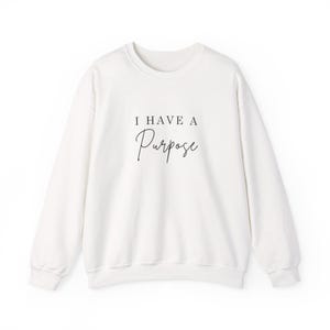 Könnte beinhalten: Weißes Sweatshirt mit Rundhalsausschnitt und dem Text "I HAVE A Purpose" in schwarzer Schrift. Das langärmlige Oberteil ist aus einem weichen Material gefertigt und eignet sich für Freizeitkleidung. Das Sweatshirt hat eine lockere Passform und ein klassisches Design.